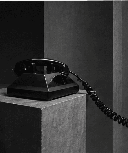 A black rotary telephone on a stone plinth, handset lifted.